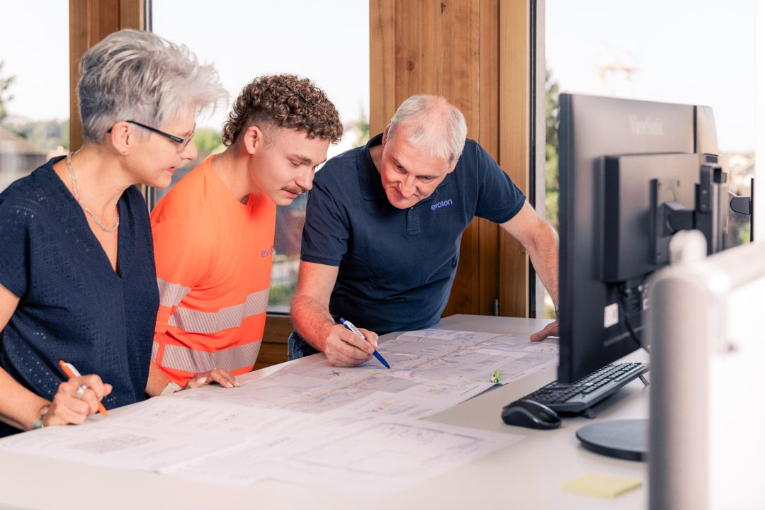 Mitarbeiterfotos Evolon AG: drei Mitarbeitende besprechen Netzpläne im Büro