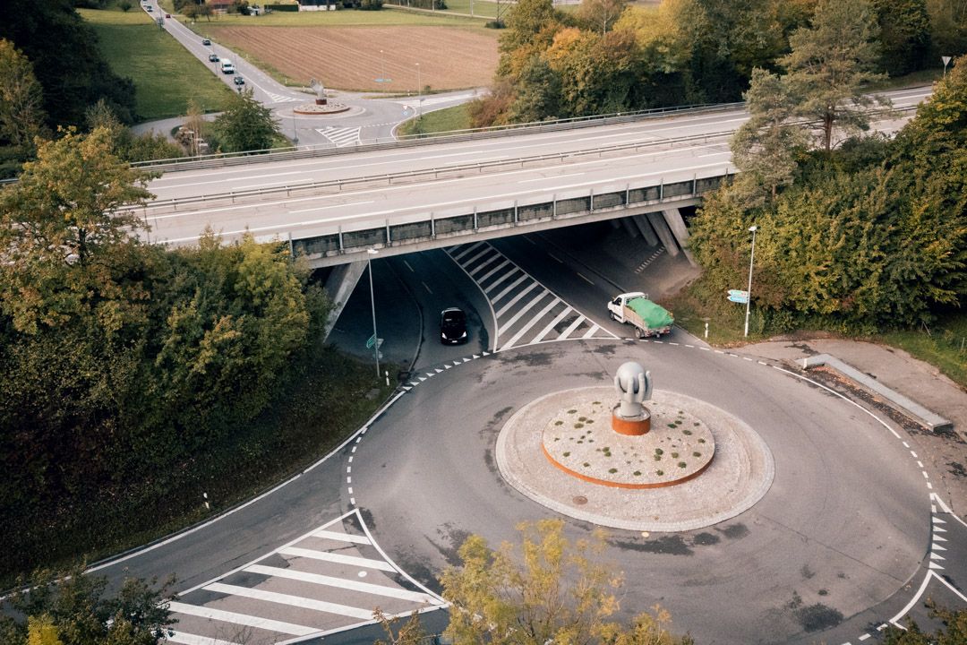 Drohnenaufnahme der Kreiselskulpturen Lyss–Aarberg an der Autobahnausfahrt Lyss Süd im Seeland: Kunst am Bau mit Hand und Chromstahlkugel im Kreisel