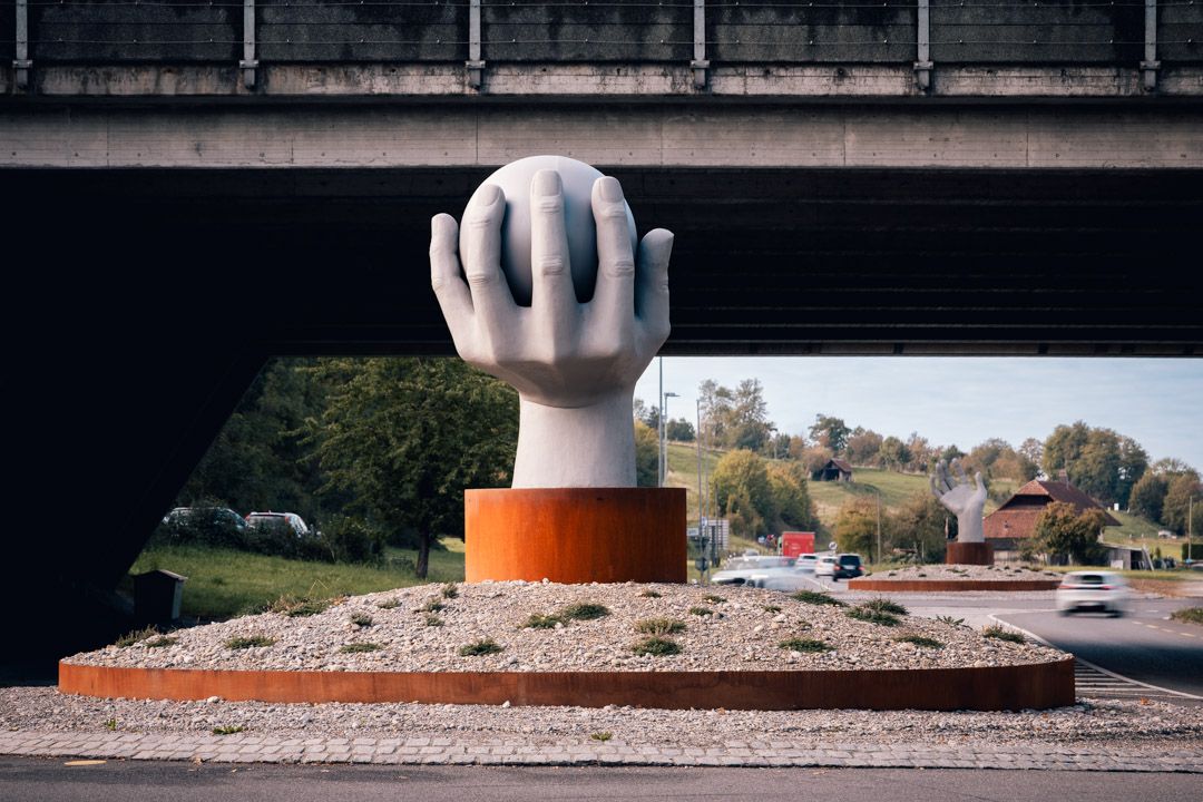 Kreiselskulpturen Lyss–Aarberg unter der Autobahnbrücke: Lysser Hand mit Chromstahlkugel vorne, Aarberger Hand im Hintergrund, Architekturfotografie im Seeland